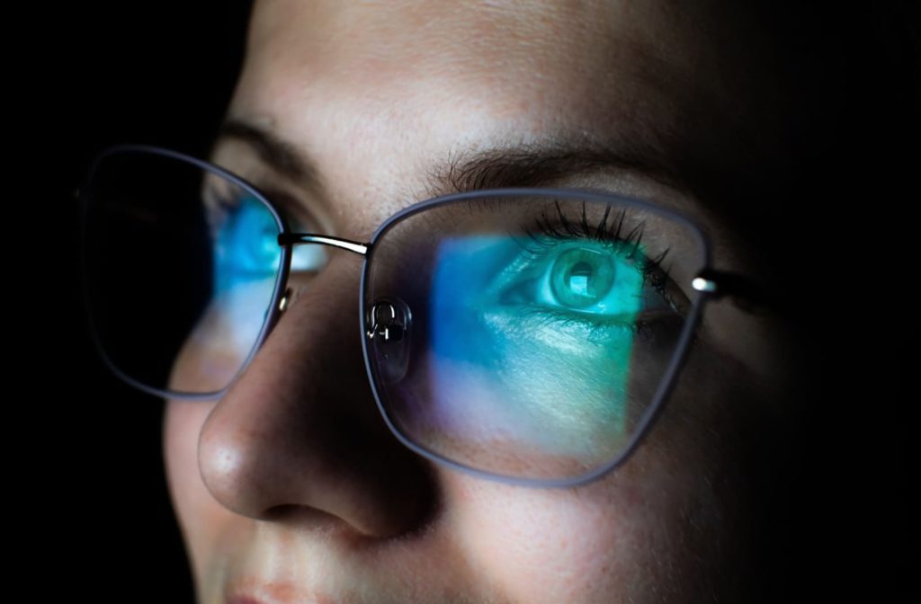 A close-up of a woman wearing blue light glasses, with the glow from the computer screen reflecting on the lenses, highlighting the protective measure against eye strain.