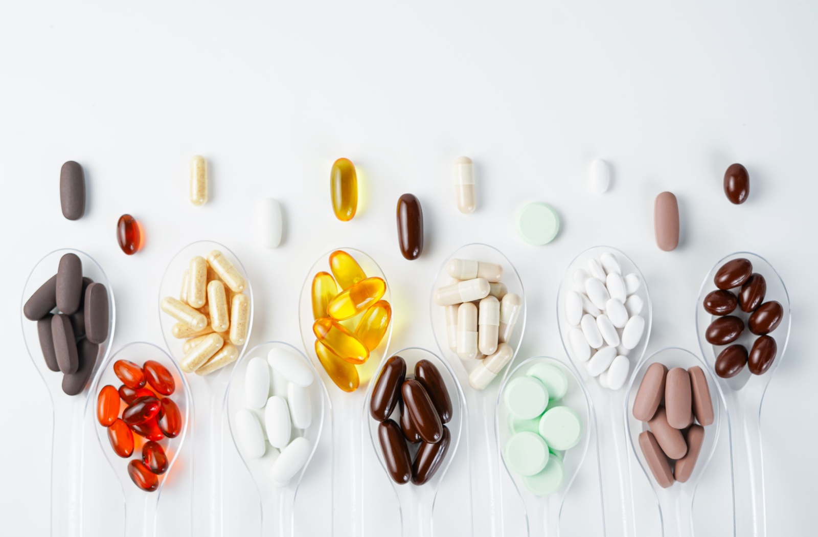 Various nutritional supplement pills stacked in a series of different clear spoons.