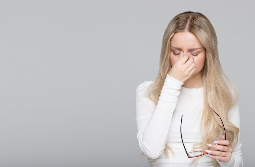 A young adult taking off their glasses to rub their eyes in frustration due to blurry vision from dry eye syndrome.