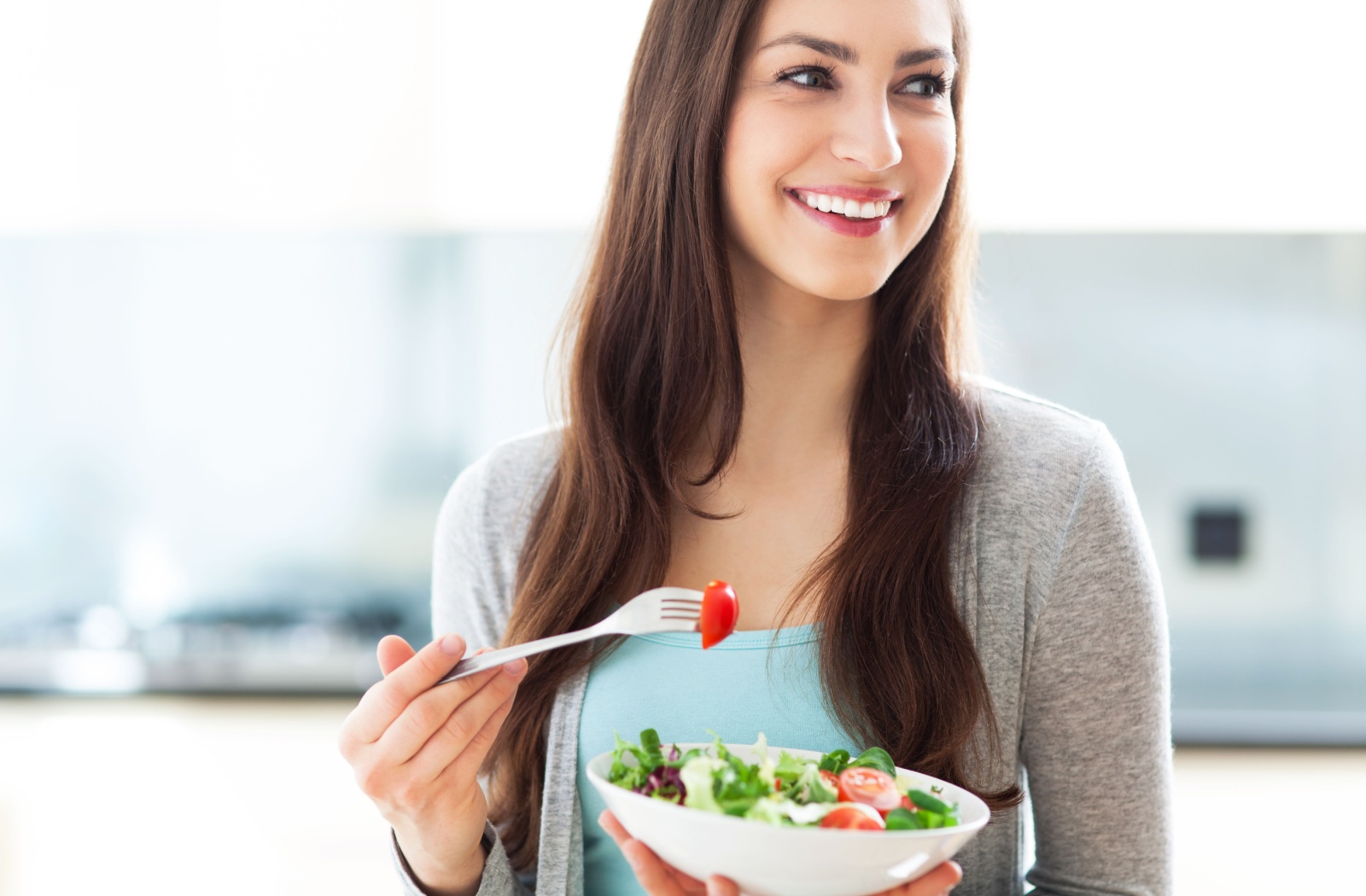 A smiling woman eats a salad.
