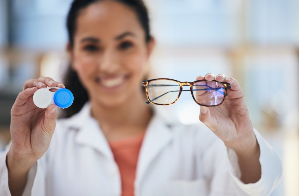 Smiling optometrist holds a pair of glasses and a contact lens case highlighting the difference between vision correction options