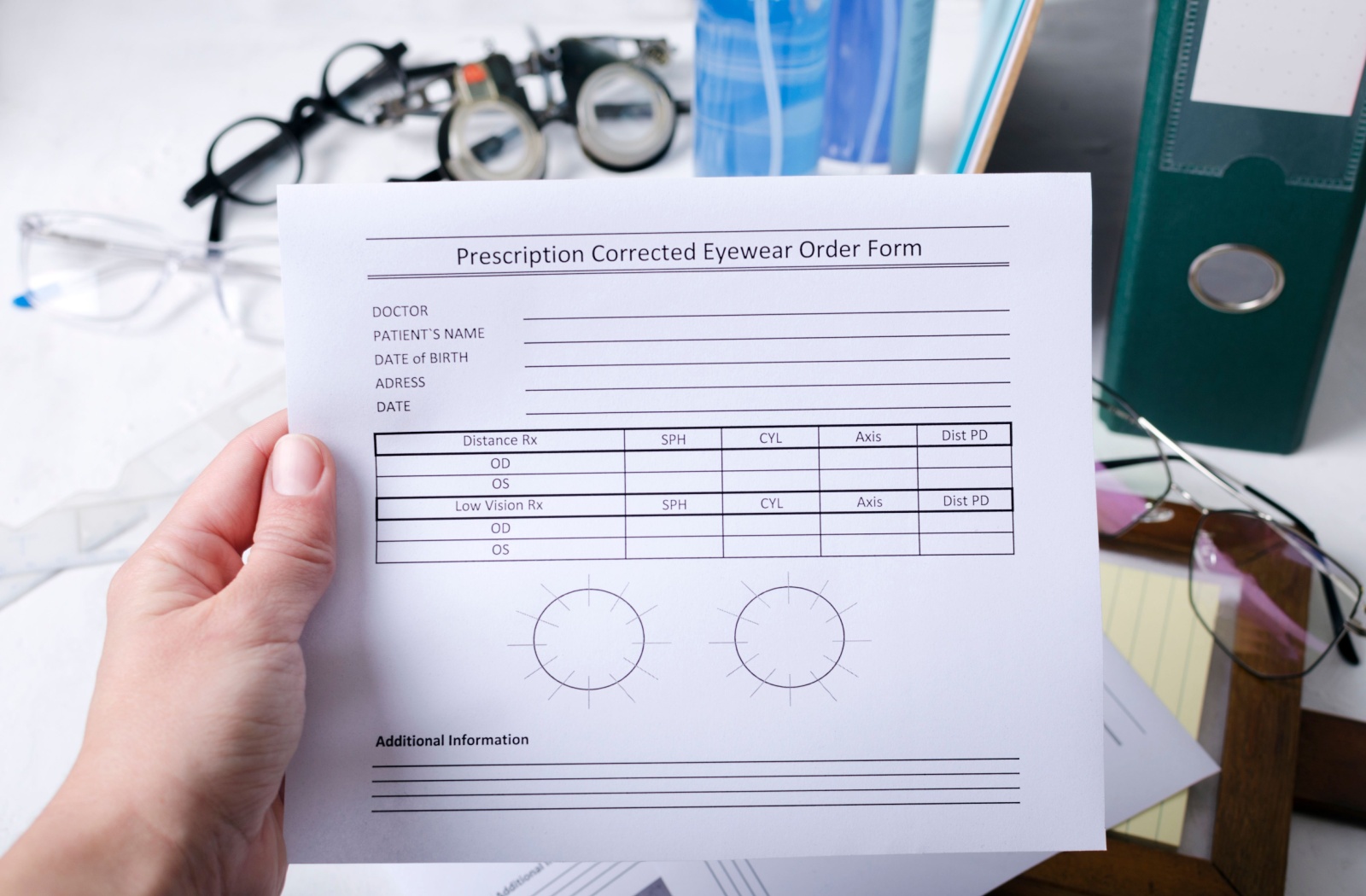 Hand holding a glasses prescription form with eyewear and optometry tools blurred in the background on a clinic desk