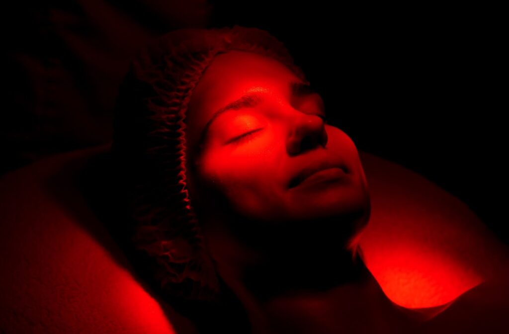 A person lies back and closes their eyes as red light shines on their face.